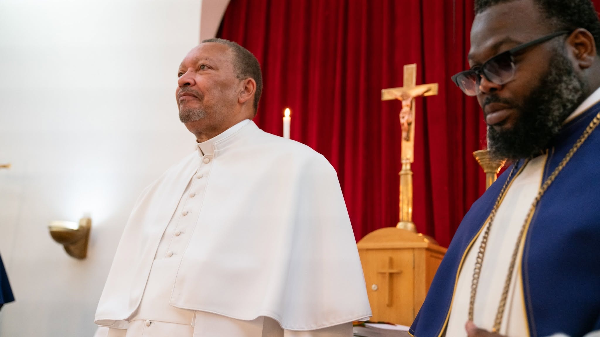 Two ministers at the altar — robed in white before the cross